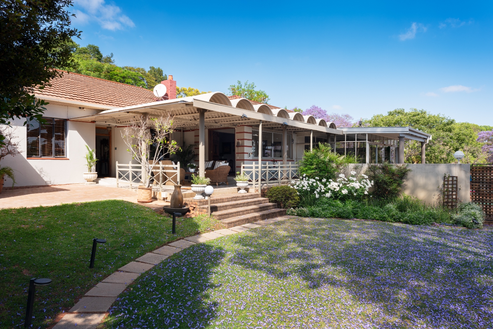 Jacaranda-shaded garden and pergola patio at the front of House Falcon Guest House in Muckleneuk