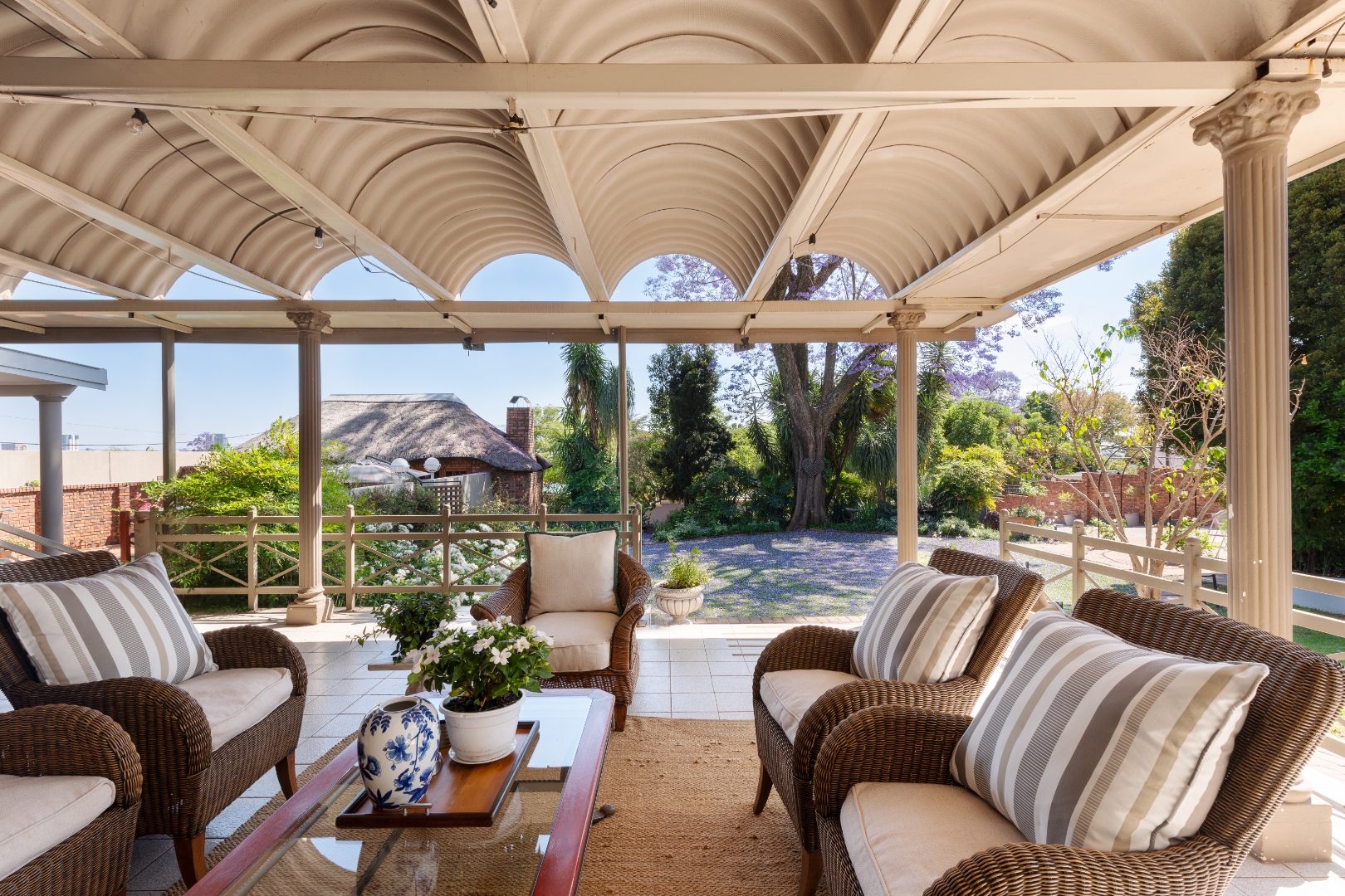 Covered verandah lounge with wicker armchairs overlooking the jacaranda garden at House Falcon Guest House, Muckleneuk